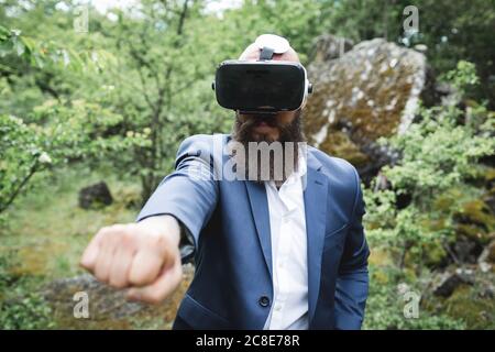 Close-up of businessman looking through virtual reality simulator while practicing martial arts in forest Stock Photo