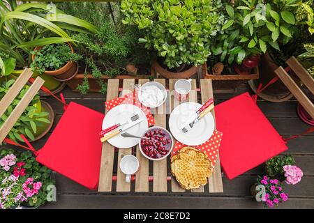 Homemade waffles on small table set on balcony surrounded by green potted herbs Stock Photo