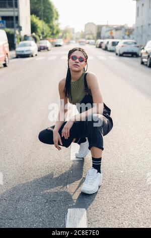 Portrait of a confident stylish young woman crouching on the street in the city Stock Photo
