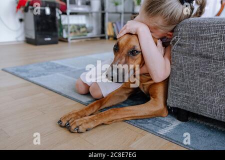Girl embracing dog while relaxing on carpet in living room at home Stock Photo