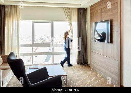 Chambermaid opening curtains of window in hotel bedroom Stock Photo