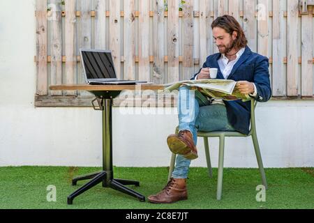 Handsome young male entrepreneur reading newspaper while drinking espresso at cafe Stock Photo