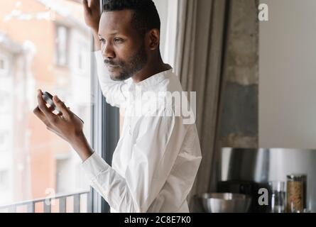 Portrait of pensive businessman with mobile phone looking out of window Stock Photo