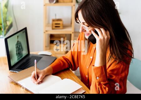 Female fashion designer working at home sitting at desk taking notes Stock Photo
