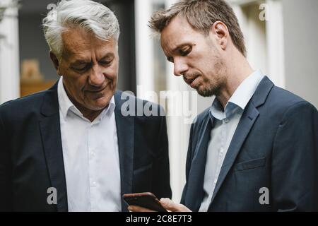 Two businessman standing in backyard, using smartphone Stock Photo