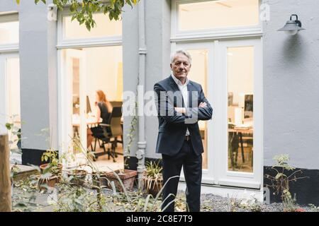 Senior businessman standing in backyard of his office with arms crossed Stock Photo