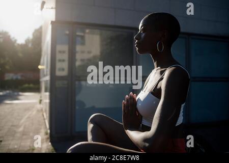 Young woman meditating while sitting outdoors in city during sunny day Stock Photo