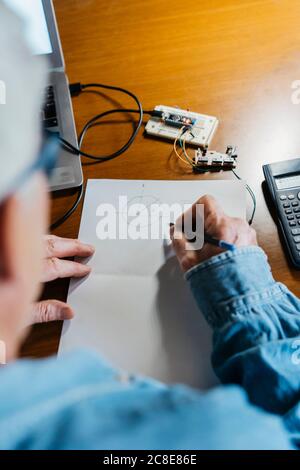 Senior man making diagram on paper while repairing laptop at home Stock Photo