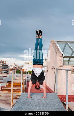 Young man doing handstand on abandoned terrace against cloudy sky
