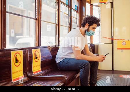 Man wearing face mask using mobile phone while sitting in tram Stock Photo