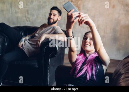 Happy young woman taking selfie with man on sofa in a loft Stock Photo