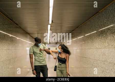 Couple wearing masks while greeting each other with elbows in underground walkway Stock Photo