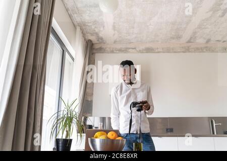 Smiling man using laptop and camera at home Stock Photo