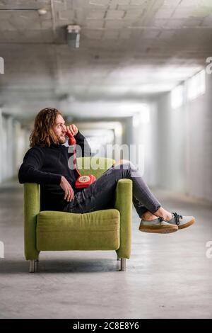Man talking over telephone while relaxing on armchair at home Stock Photo