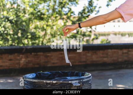 Hand of woman holding protective mask over garbage bin in city Stock Photo