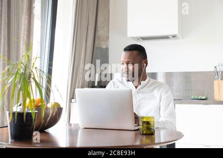 Portrait of man using laptop and earphones at home Stock Photo
