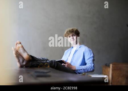 Portrait of relaxed young man with feet on table using digital tablet Stock Photo