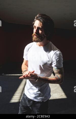 Thoughtful bearded man standing against built structure on sunny day Stock Photo