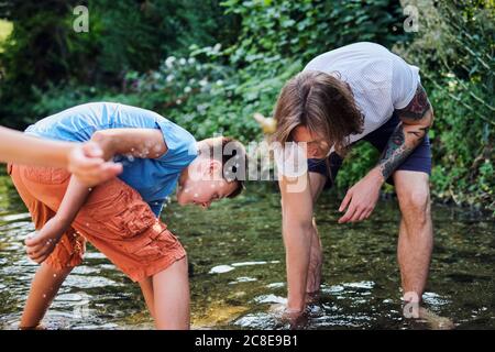 Man exploring with boy in stream water at forest Stock Photo