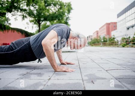 Active senior man doing push-ups on footpath in city Stock Photo