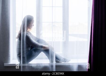 Young woman sitting on window at home Stock Photo