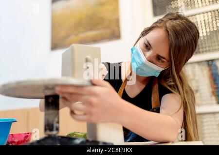 Close-up of young woman wearing mask making pottery in studio Stock Photo