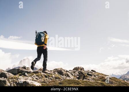 Man with backpack walking on mountain against sky during sunny day, Patagonia, Argentina Stock Photo