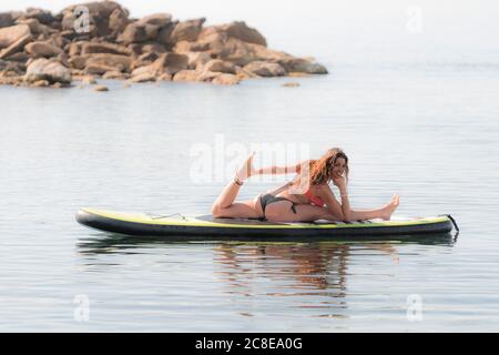 Smiling flexible woman practicing yoga on paddleboard Stock Photo