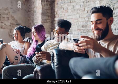 Group of friends sitting on sofa in a loft using smartphones Stock Photo