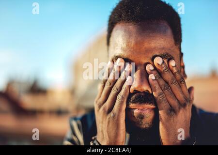 Close-up of young man with hands covering eyes on rooftop in city