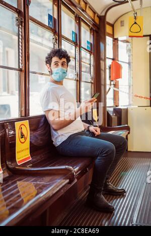 Young man wearing mask using smart phone while sitting in tram Stock Photo