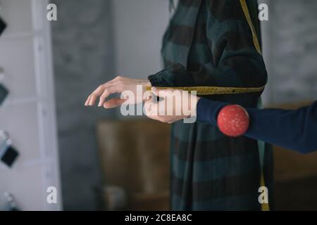 Cropped hands of tailor measuring woman's hand in design studio Stock Photo