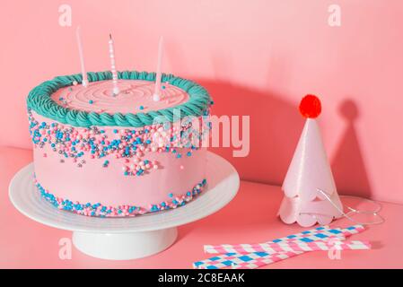 Cake stand with strawberry birthday cake, drinking straws and party hats