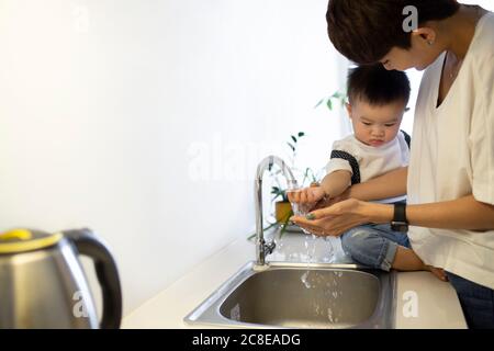 Mother washing cute son's hands in kitchen sink at home Stock Photo