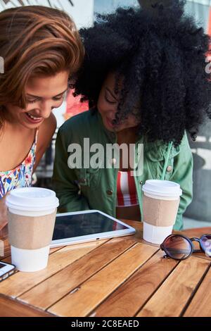Girlfriends with coffee to go using tablet in cafe Stock Photo