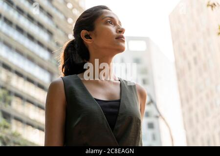 Close-up of thoughtful woman looking away while standing in modern city Stock Photo
