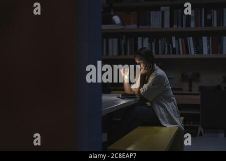 Young woman sitting in office, reading book at night with a torch Stock Photo