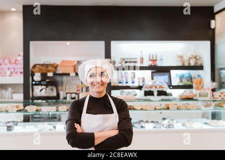 Happy female baker standing arms crossed at bakery Stock Photo