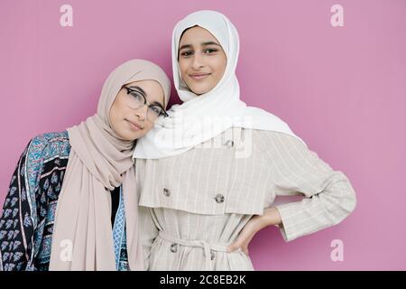 Muslim sisters standing together against purple background Stock Photo