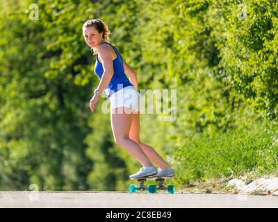 Young woman skateboarding on road by plants during sunny day Stock Photo