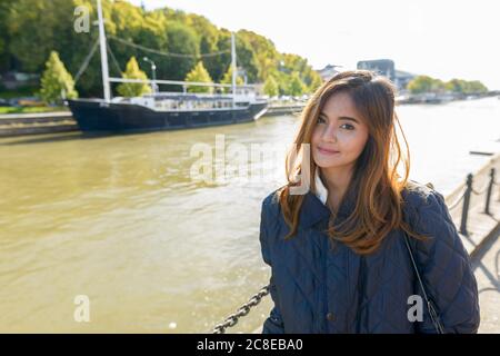 Young beautiful Asian woman standing in pier with vintage black boat in the river Stock Photo