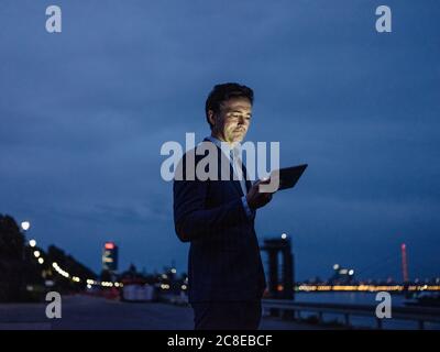 Mature businessman using tablet at the riverbank at dusk Stock Photo