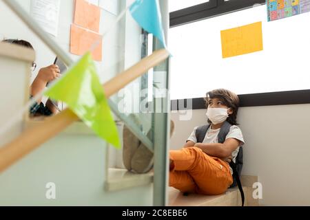 Boy wearing mask looking at friend using digital tablet while on steps in school Stock Photo