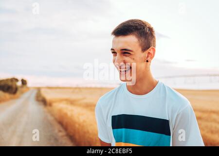 Cheerful teenage boy looking away while standing against landscape during sunset Stock Photo