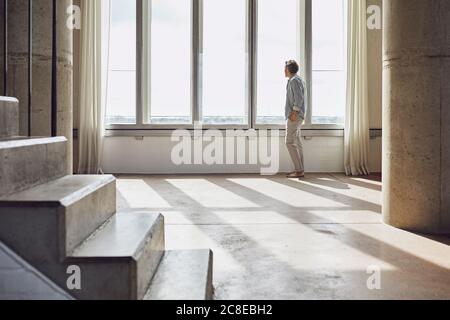 Senior man looking out of window in a loft flat Stock Photo