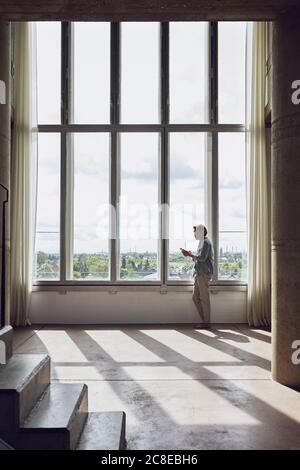 Senior man using smartphone at the window in a loft flat Stock Photo