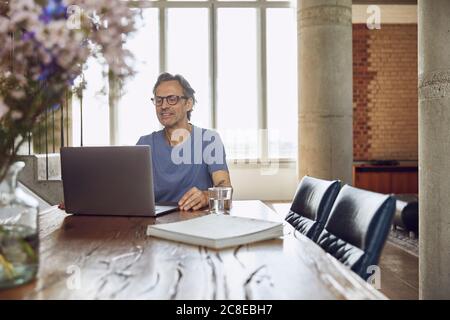 Senior man sitting at the table in a loft flat using laptop Stock Photo