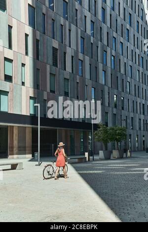 Woman walking with bicycle on city street during sunny day Stock Photo