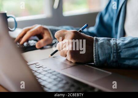 Cropped image of senior man using calculator and laptop while writing with pencil at home Stock Photo