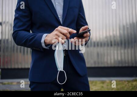Businessman with protective face mask using smartphone in the city Stock Photo